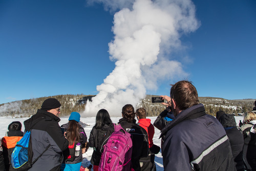 Group of visitors watching Old Faithful erupt in winter
