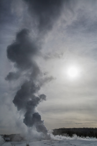 Old Faithful geyser steaming in low autumn light