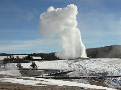 Old Faithful erupting in winter with snow-covered Old Faithful Inn