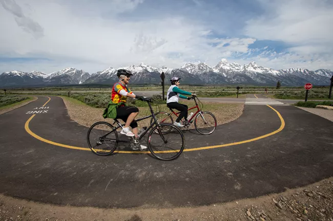 Cyclists on a paved path with Teton mountains in background
